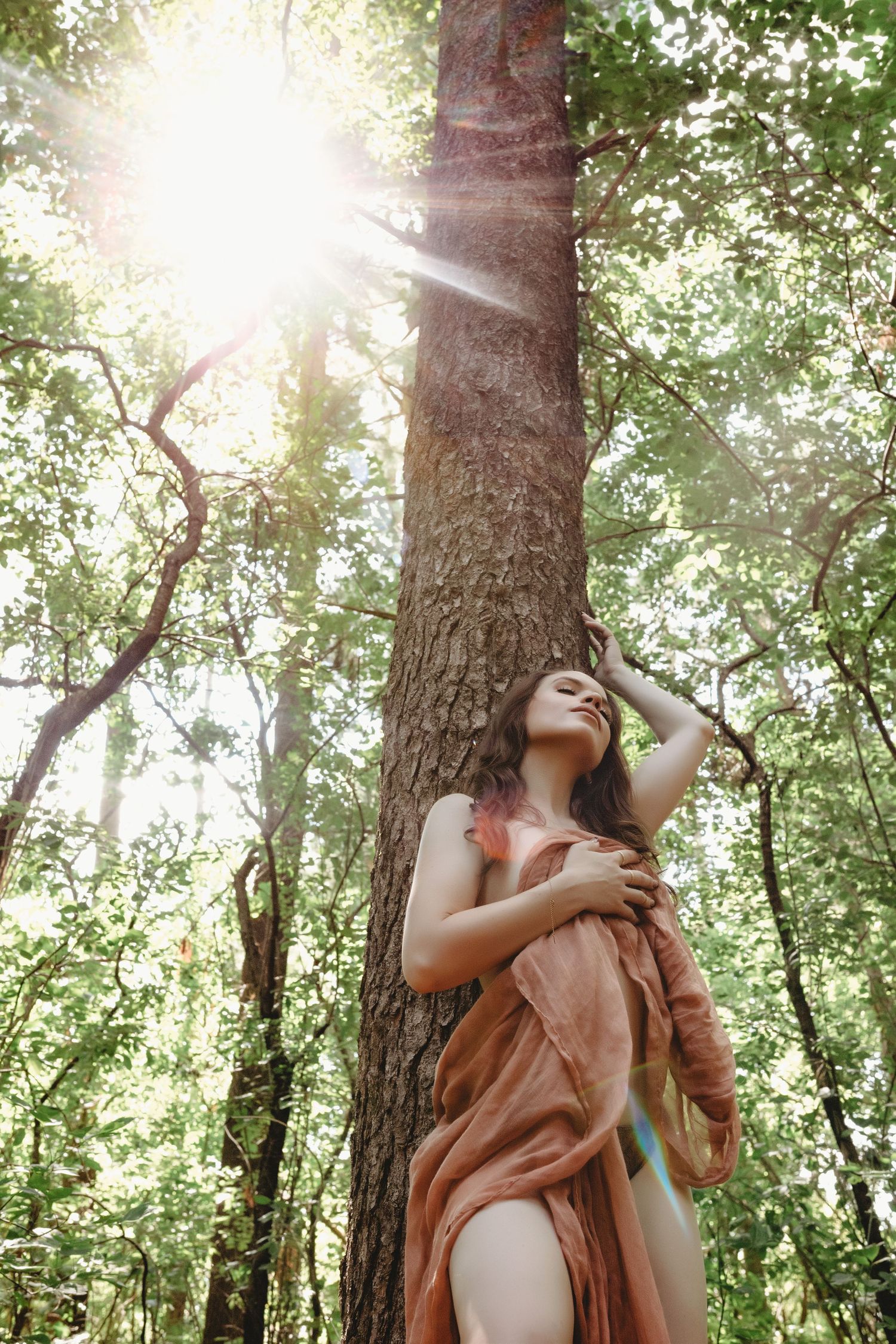 A woman in the woods, sunlight beaming during  boudoir session.