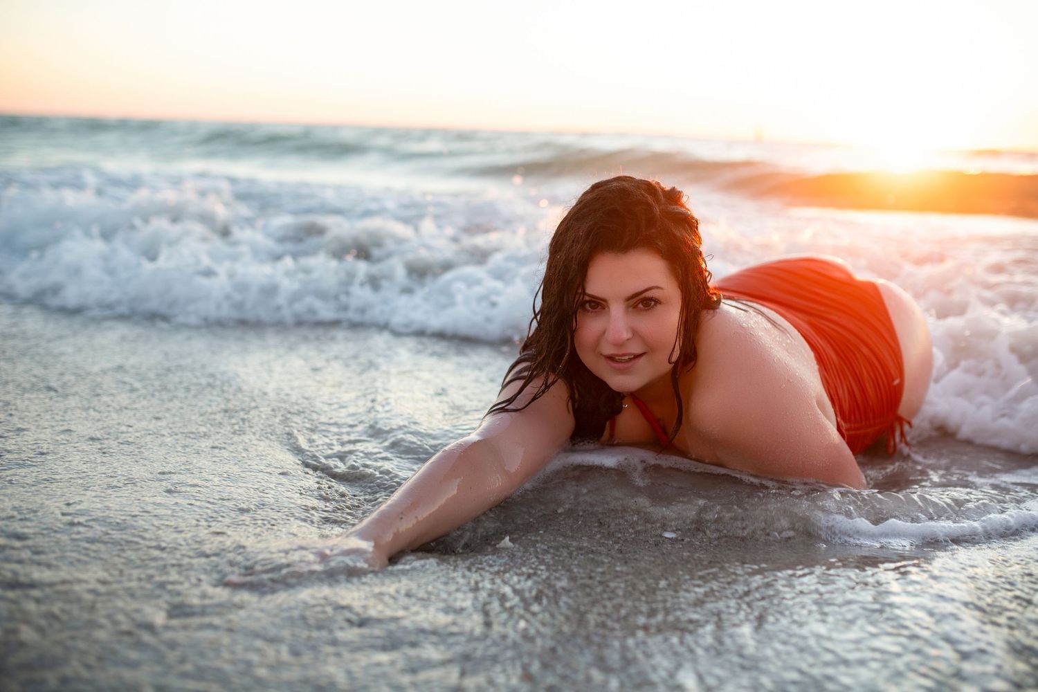 Beach boudoir photography session at sunset featuring woman posing in ocean waves.