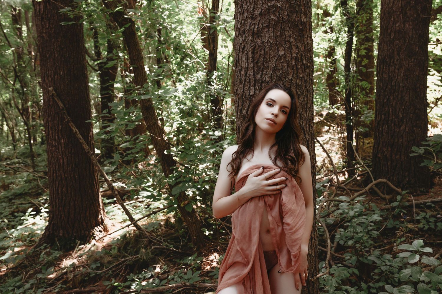 Outdoors boudoir session of a woman in the woods with a sheer cover.