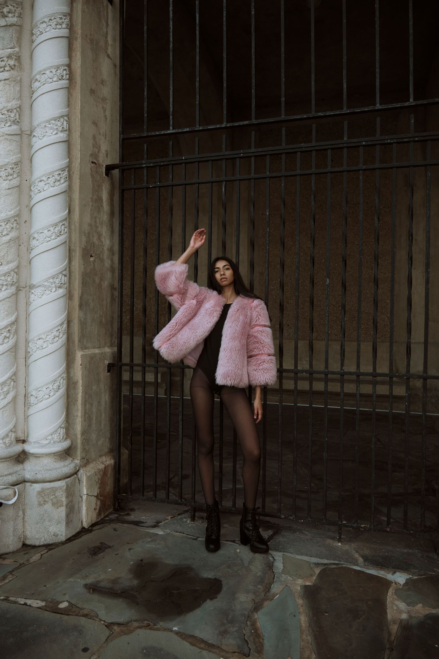 Fashion photo featuring pink fluffy jacket against industrial metal bars and columns in moody lighting.