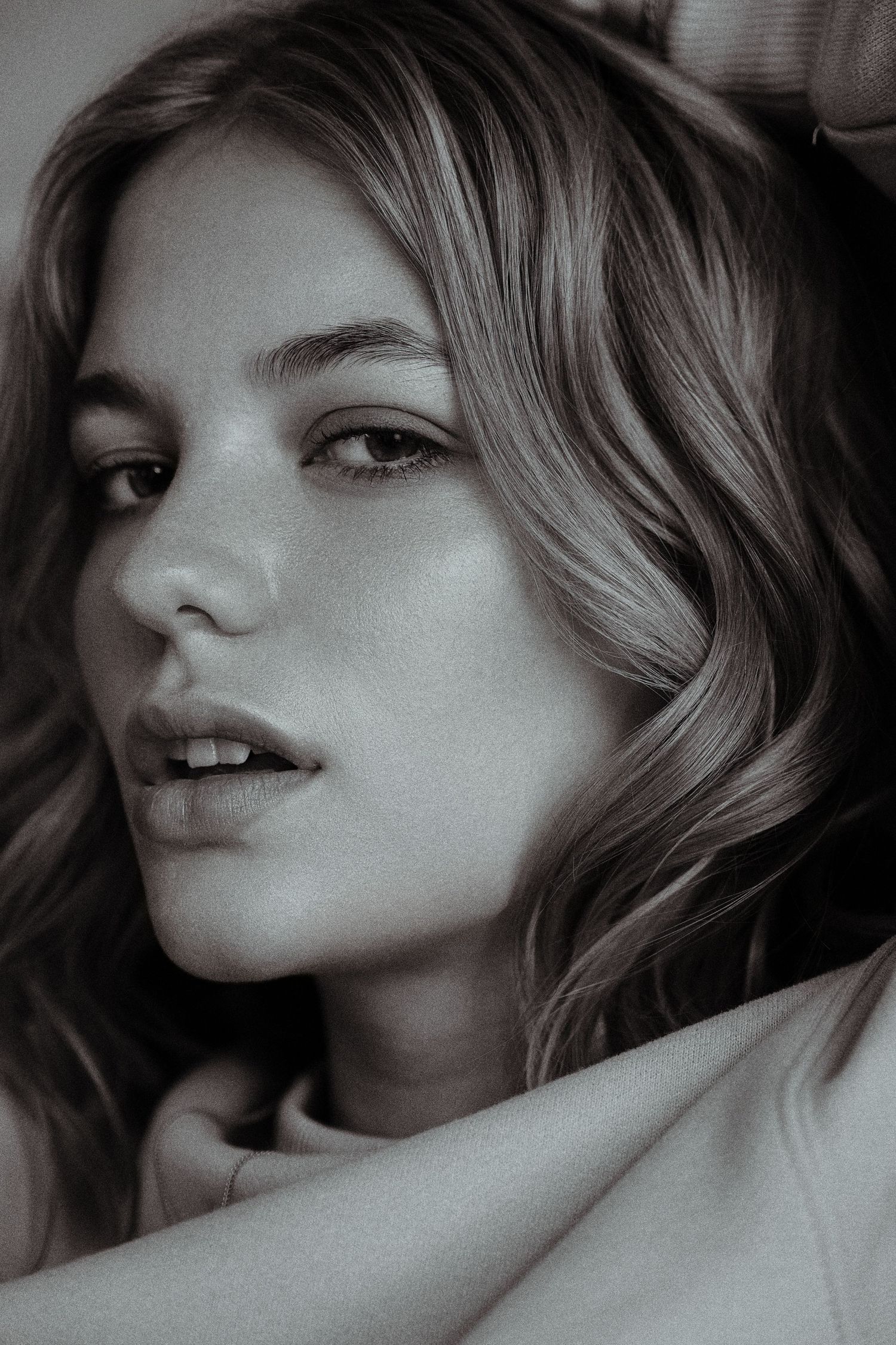 Black and white close-up portrait of a young woman with wavy hair and a soft, contemplative expression.