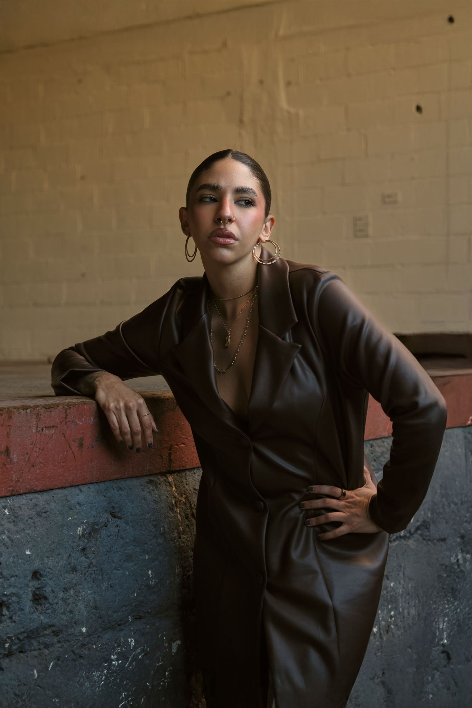 Model in dark leather jacket poses dramatically against beige wall and concrete floor.