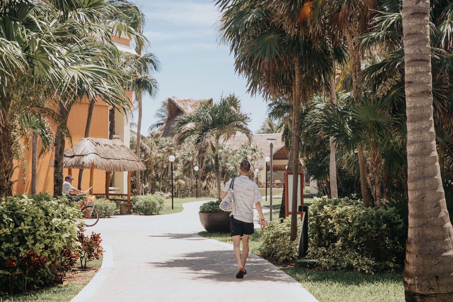 Palm-lined pathway through tropical resort grounds with orange buildings.