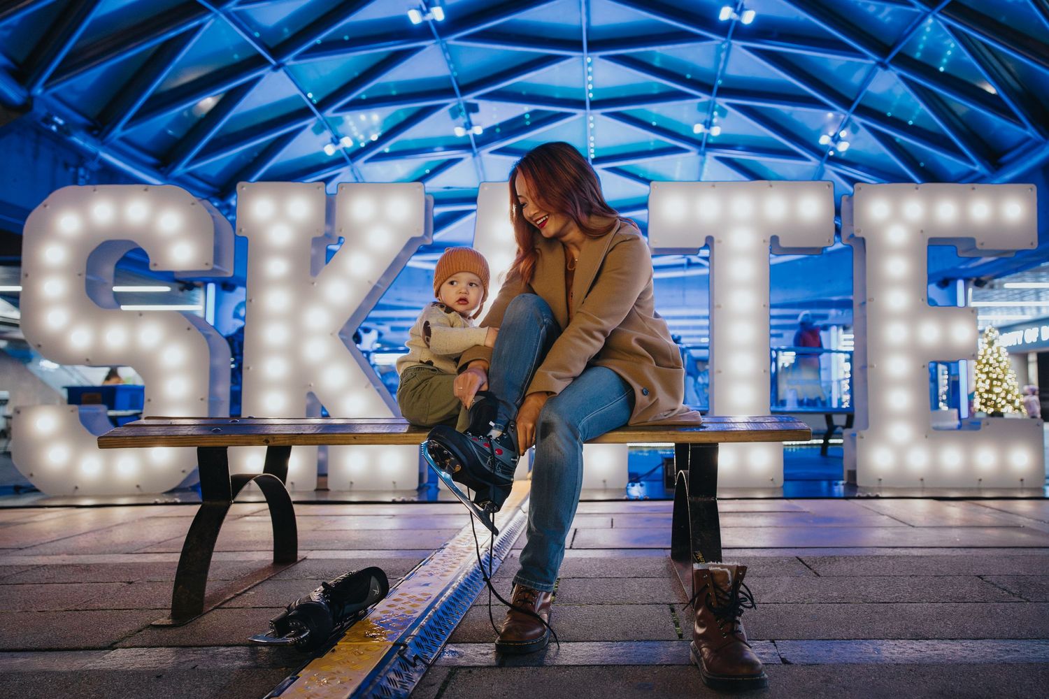 Ice skaters gliding under blue-lit dome with illuminated SKATE letters.