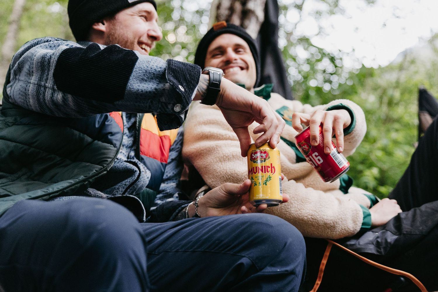 Hands holding beverages while camping outdoors in nature.