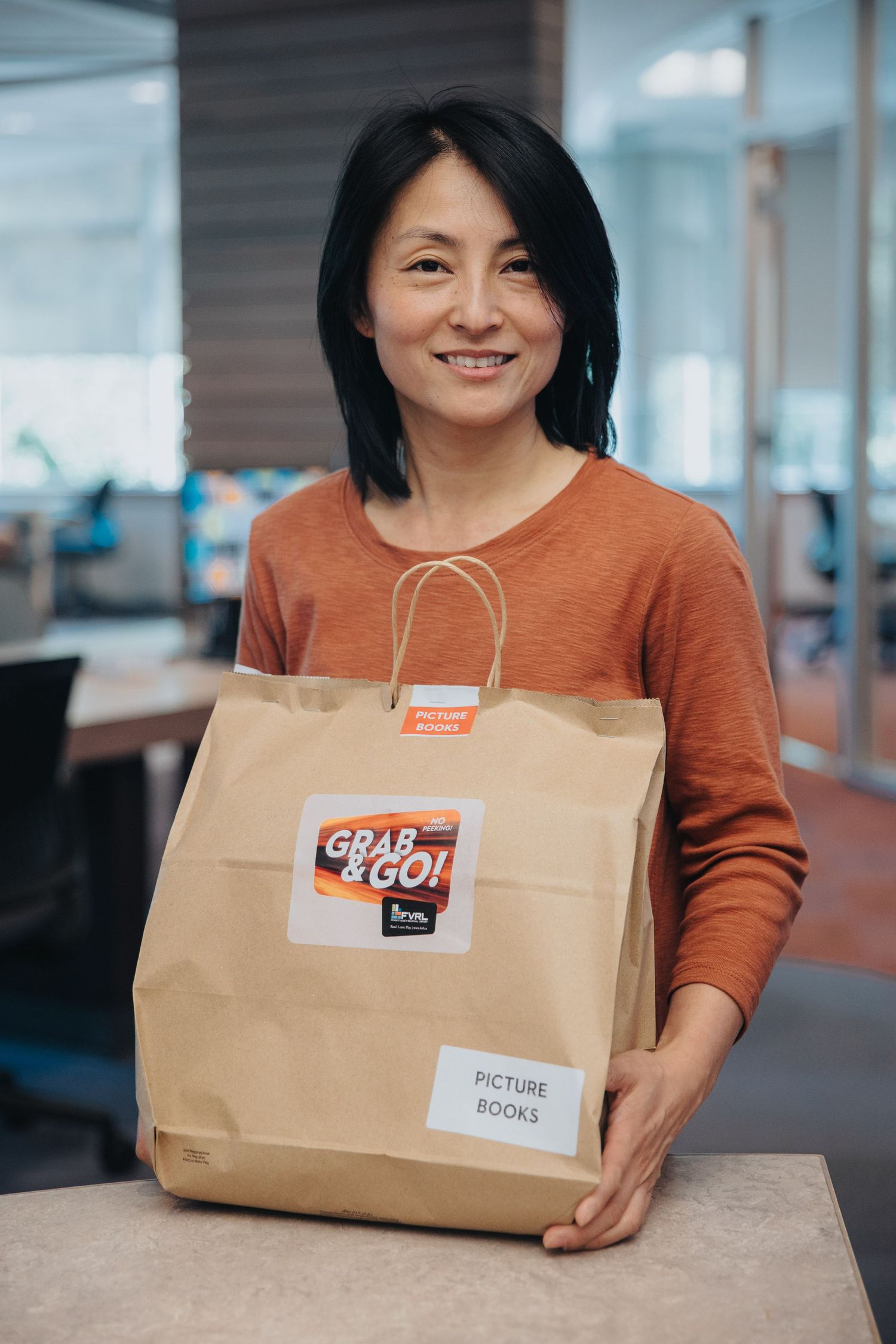 Person in orange sweater holding brown paper delivery bags with labels.