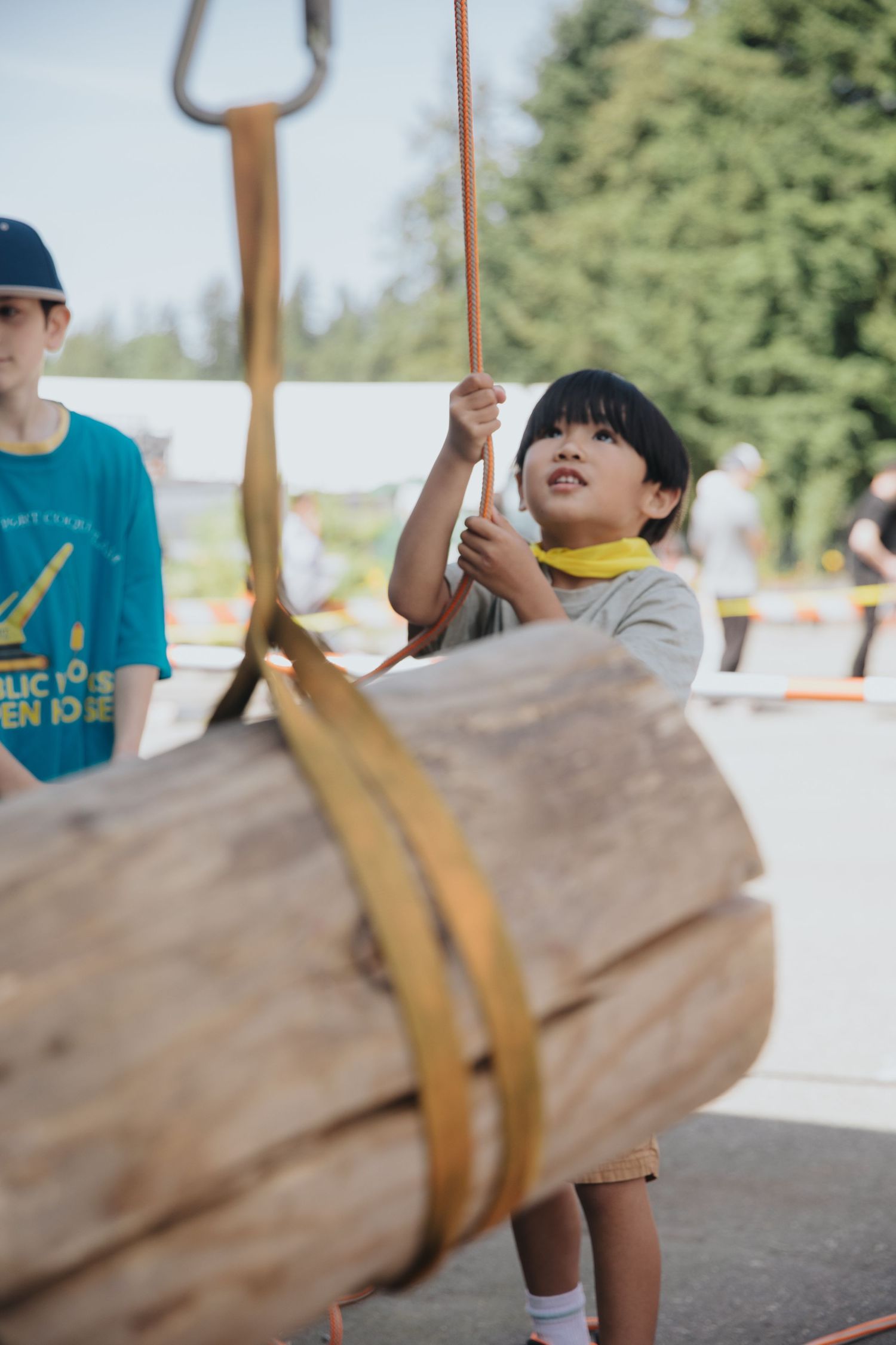 Children participating in a log-lifting activity at an outdoor event.