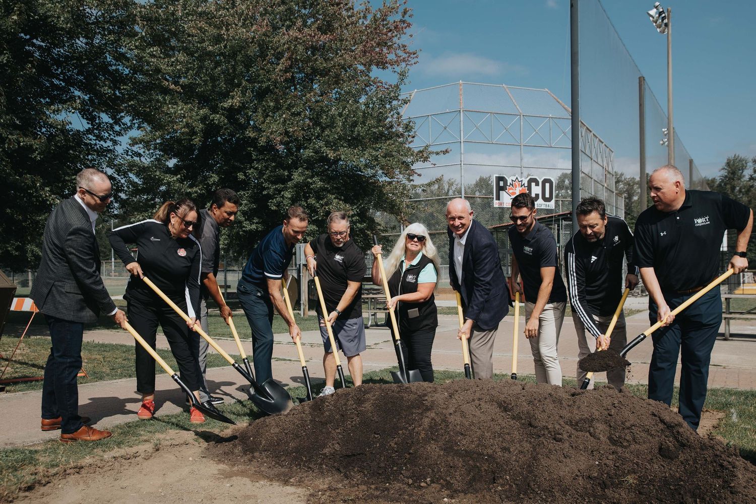 Group of people participating in ceremonial groundbreaking with shovels at outdoor event.