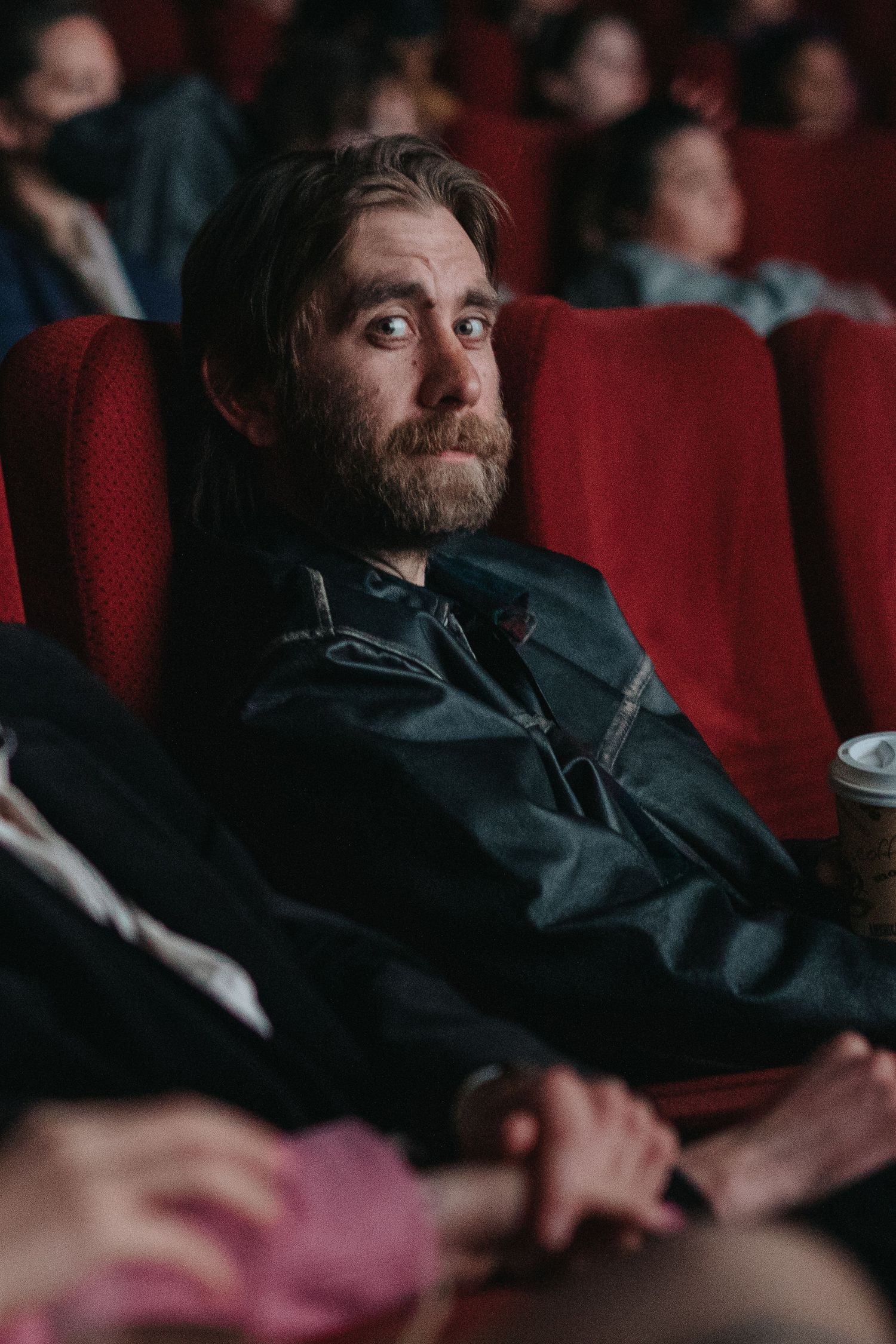 Person sitting in a dark movie theater with red seats watching a film.