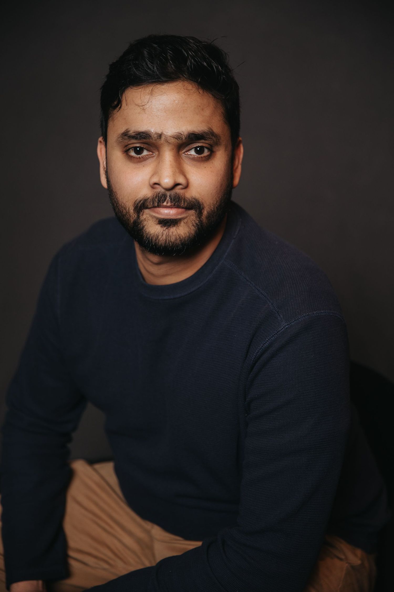 A person in a navy blue sweater poses against a dark background in a series of professional headshots.