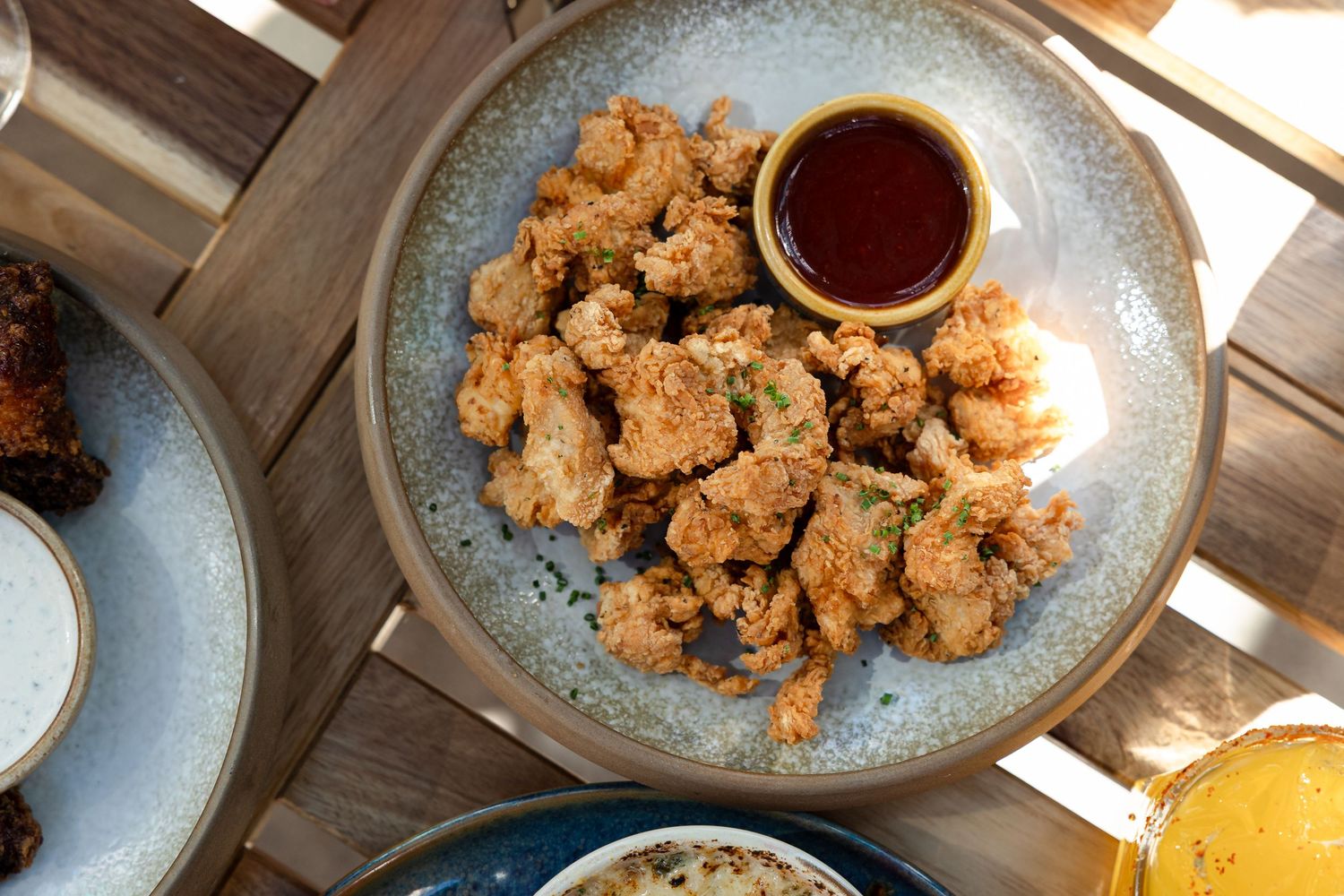 Crispy fried chicken pieces on a speckled blue plate with dipping sauce, served on a wooden table.
