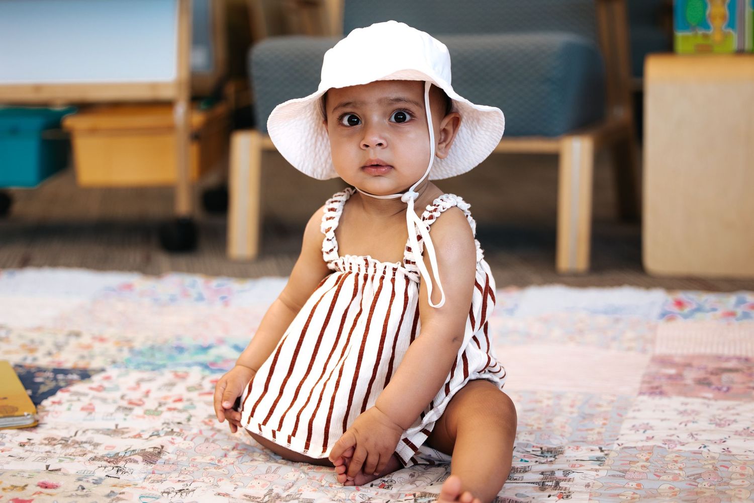 Child wearing a white sun hat plays on a carpeted floor with colorful toys.