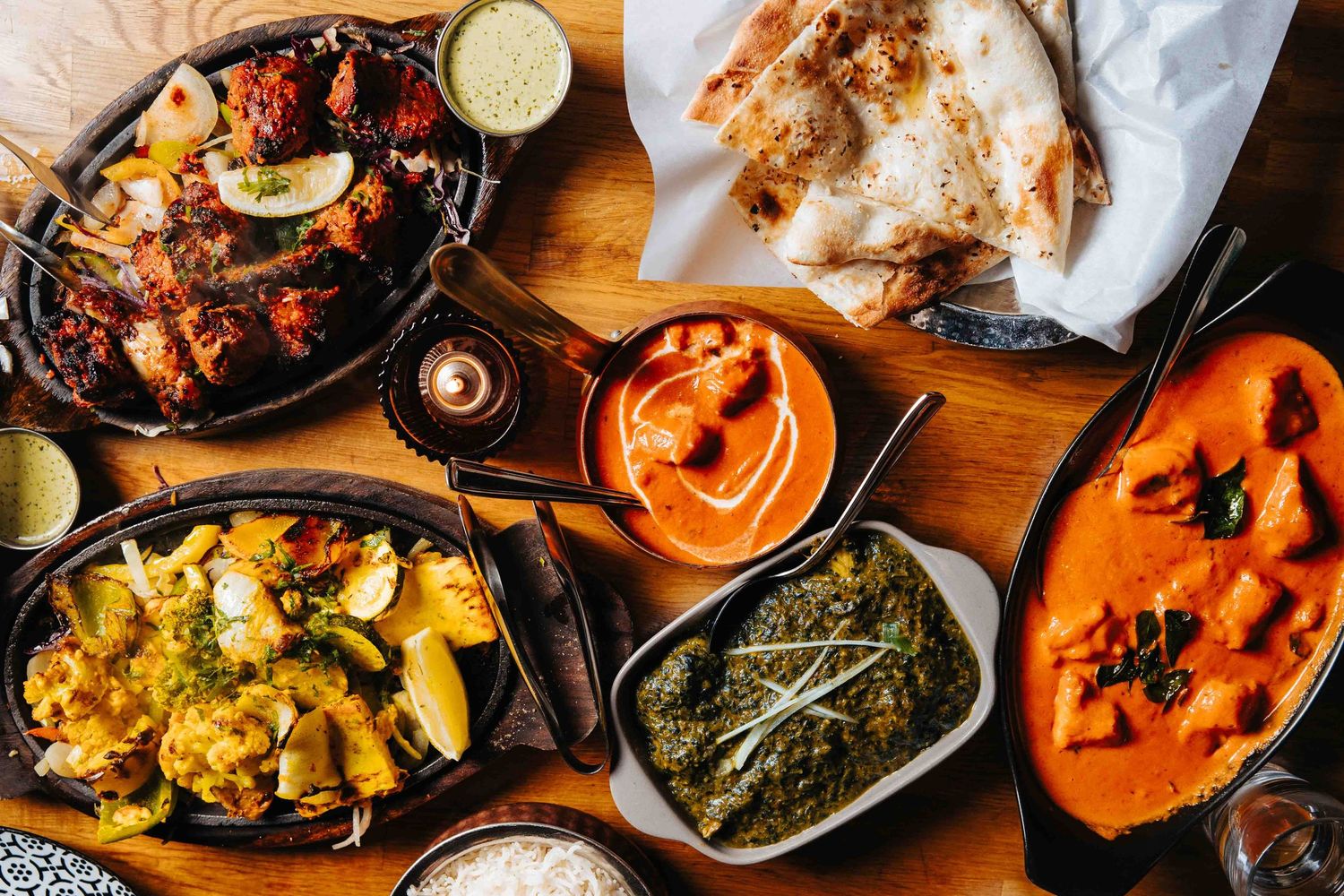 Variety of Indian curry dishes and appetizers served on wooden table at restaurant.