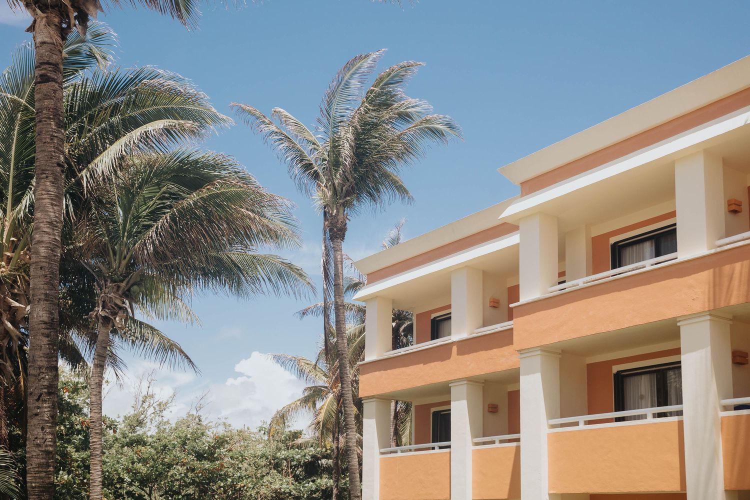 Exterior view of tropical resort showing balconies and palm trees against blue sky.
