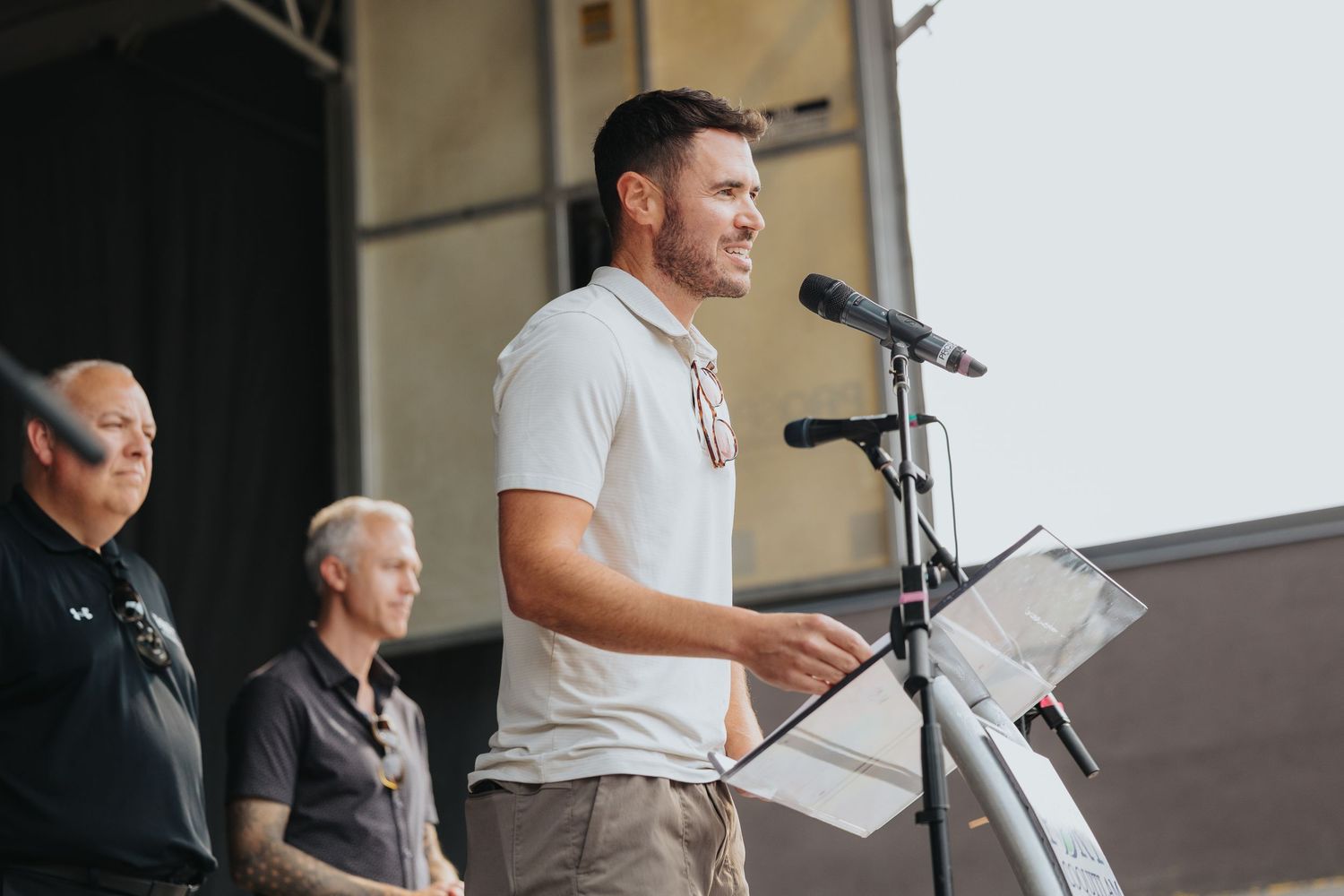 Speaker addressing audience from outdoor podium during daytime event.