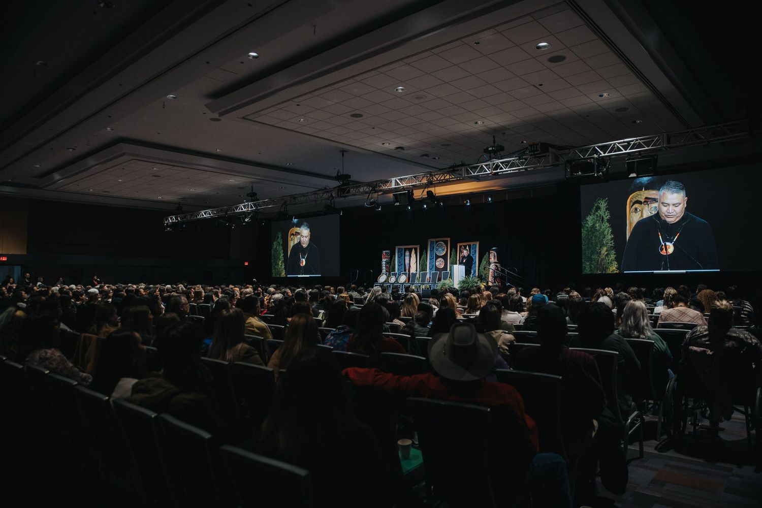 Dark auditorium filled with conference attendees during presentation.