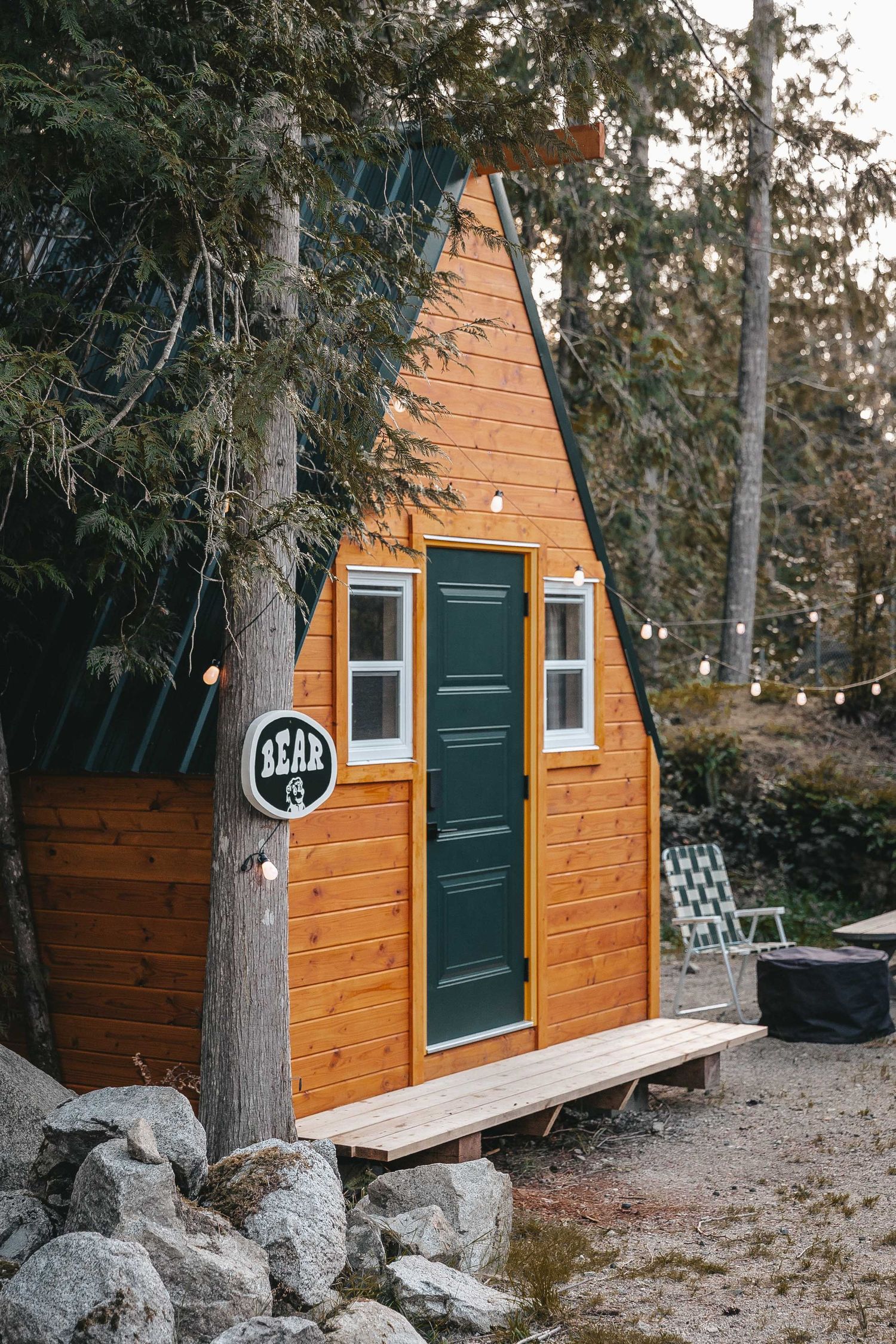 A-frame wooden cabin with green door nestled among trees in the woods.
