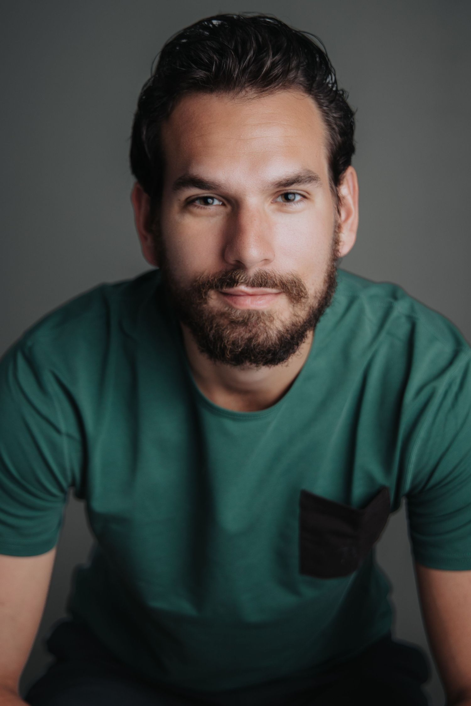 Portrait series of person in green t-shirt with beard against dark background.