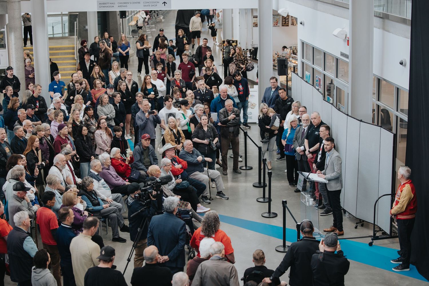 Long line of people waiting in an indoor venue with white walls and bright lighting.
