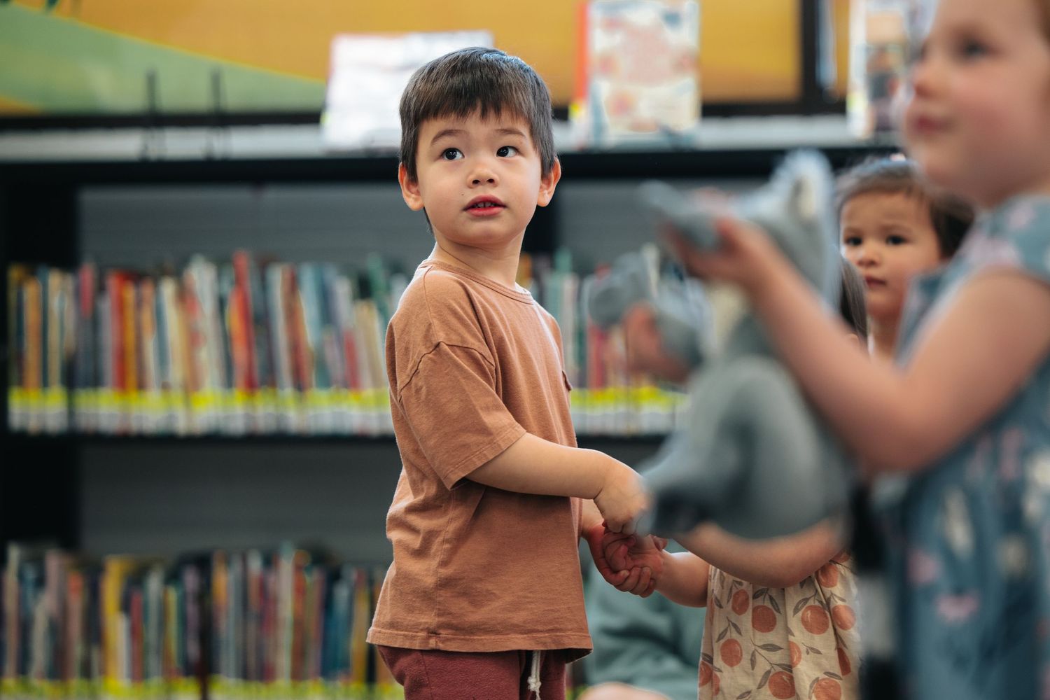 Child in a brown shirt looking attentively in a library setting.
