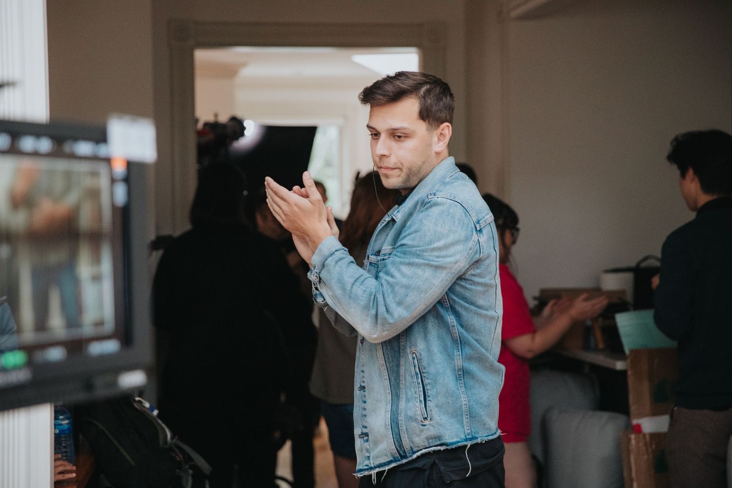 Man in denim jacket clapping on a film set with crew members and equipment in the background.