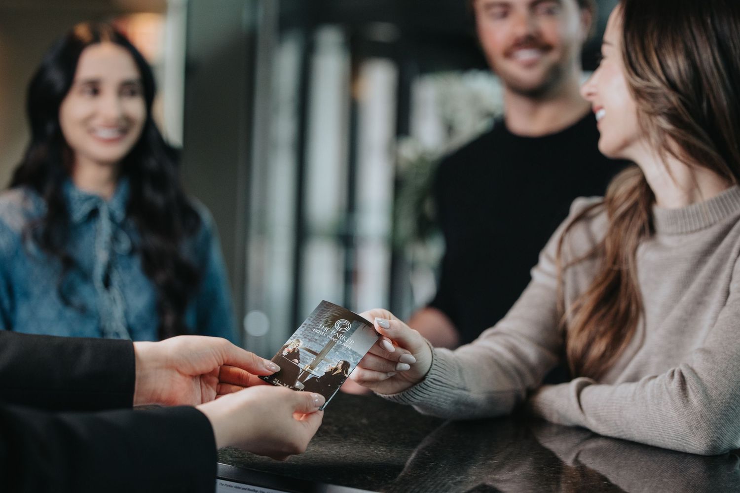 Couple checking into hotel, smiling as receptionist hands over key card at front desk.