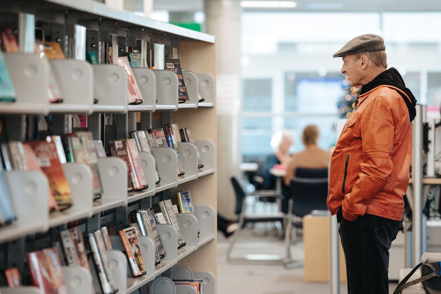 Person in orange jacket browsing books on library shelves.