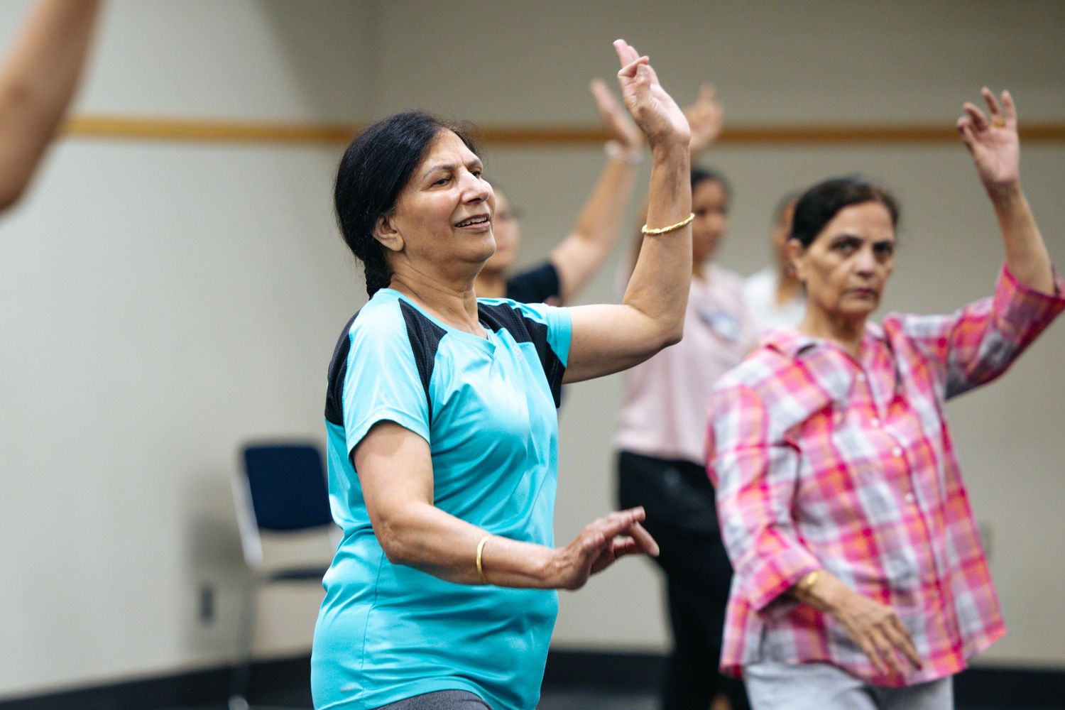 Group of participants in a dance fitness class with raised arms in a studio.