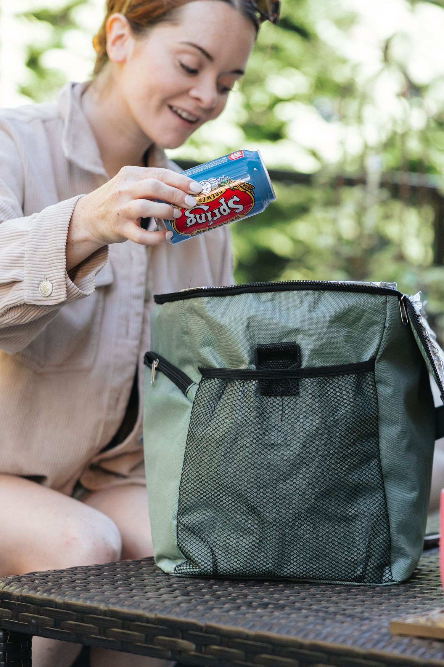 Organizing beverages into a green mesh storage bag outdoors.