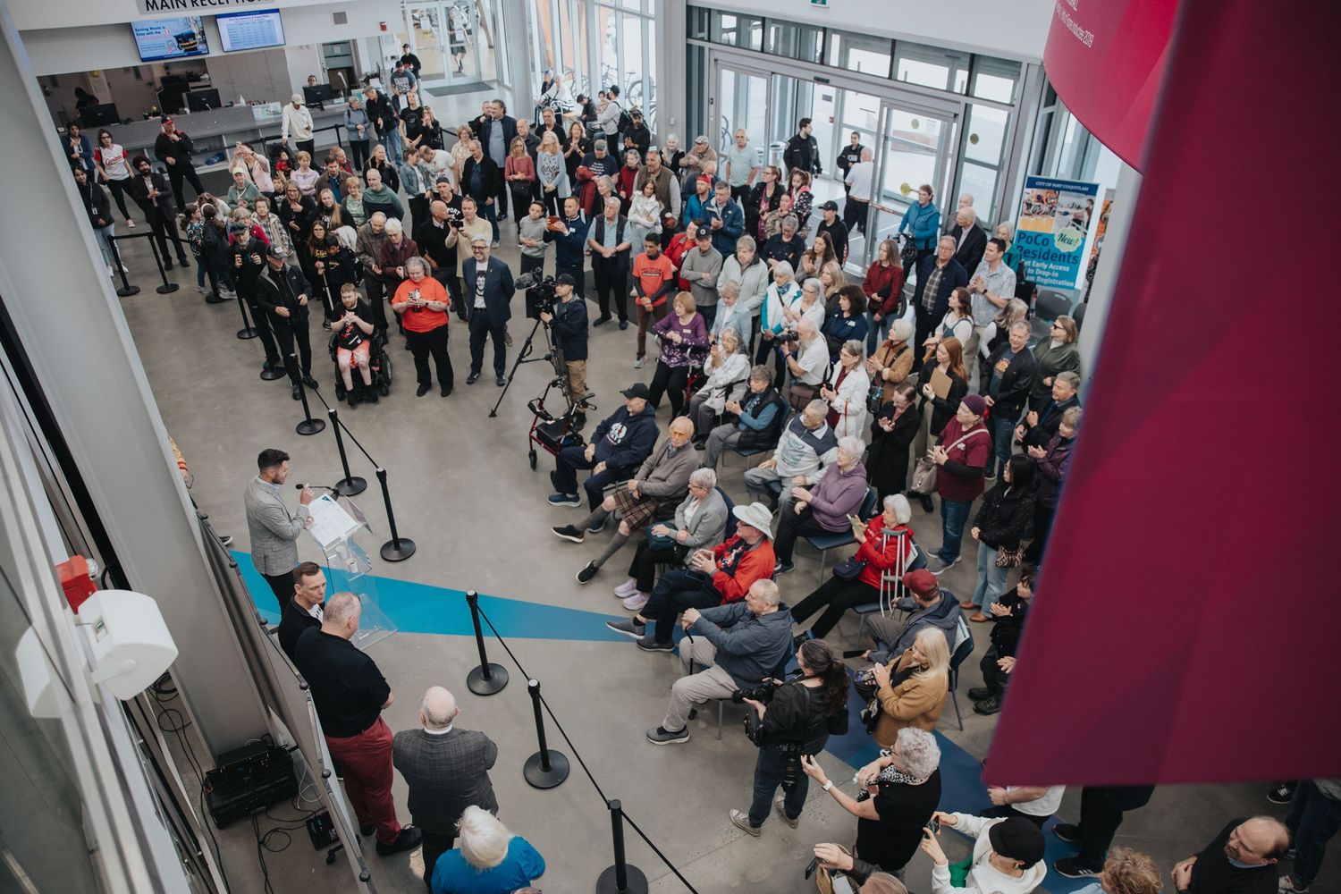 Large crowd of people gathered inside a modern building lobby or community center.