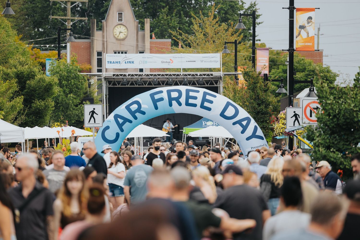 Large crowd gathered under Car Free Day arch banner at street festival.