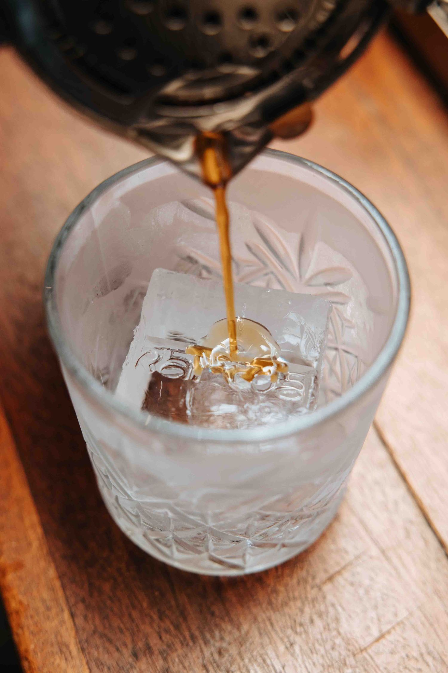 Golden liquid being poured into an ornate cut glass bowl on a wooden surface.
