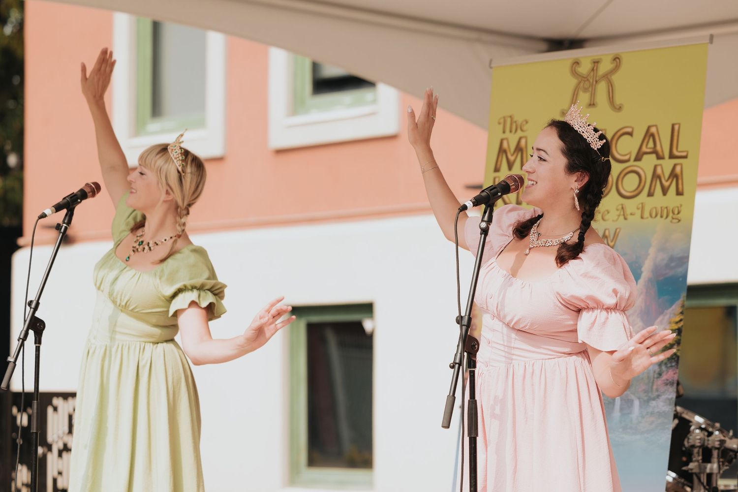 Performers in pastel dresses singing on stage at an outdoor event.