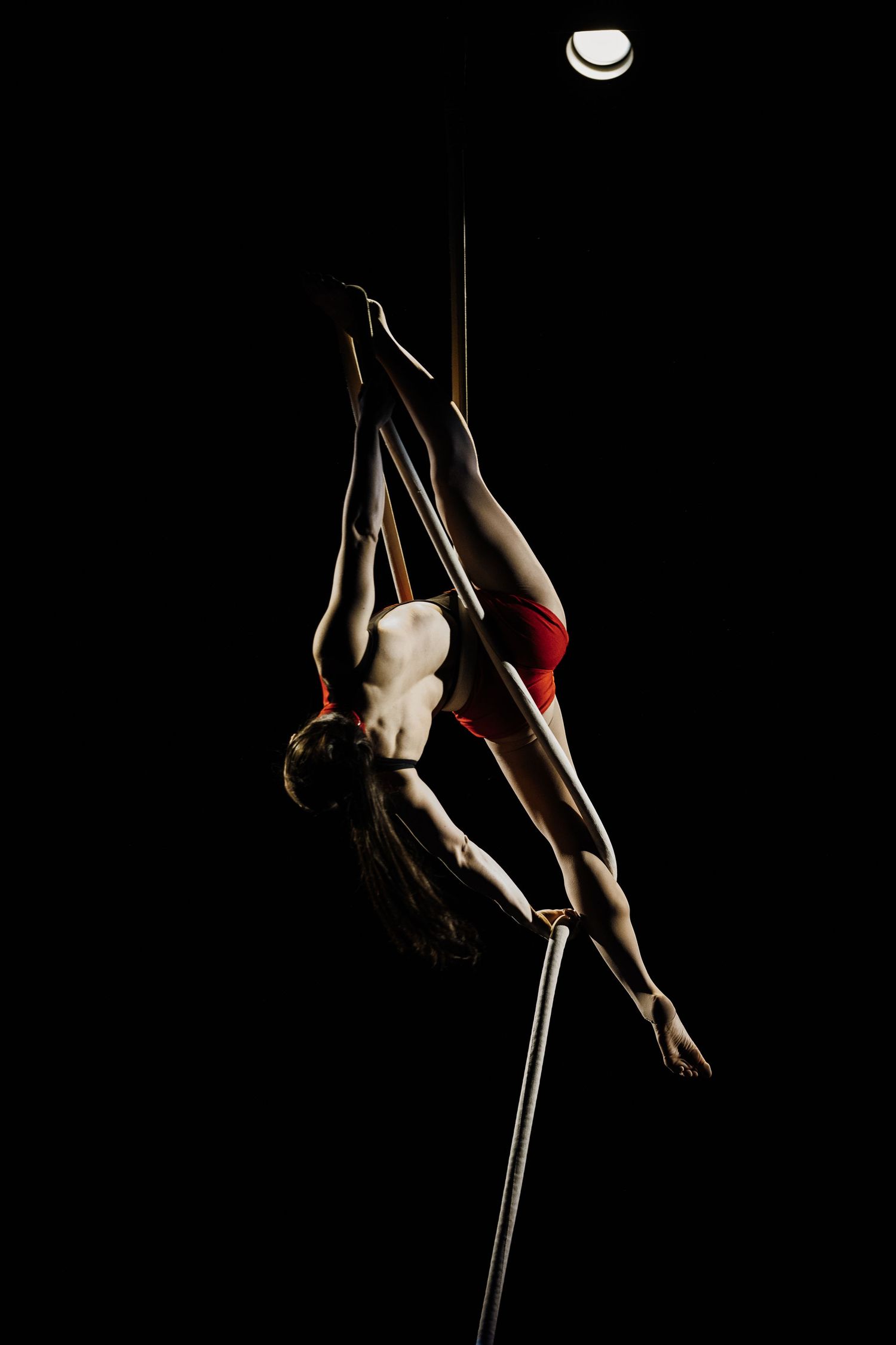 Dramatic pole dance performance sequence showing graceful aerial movements against dark background.