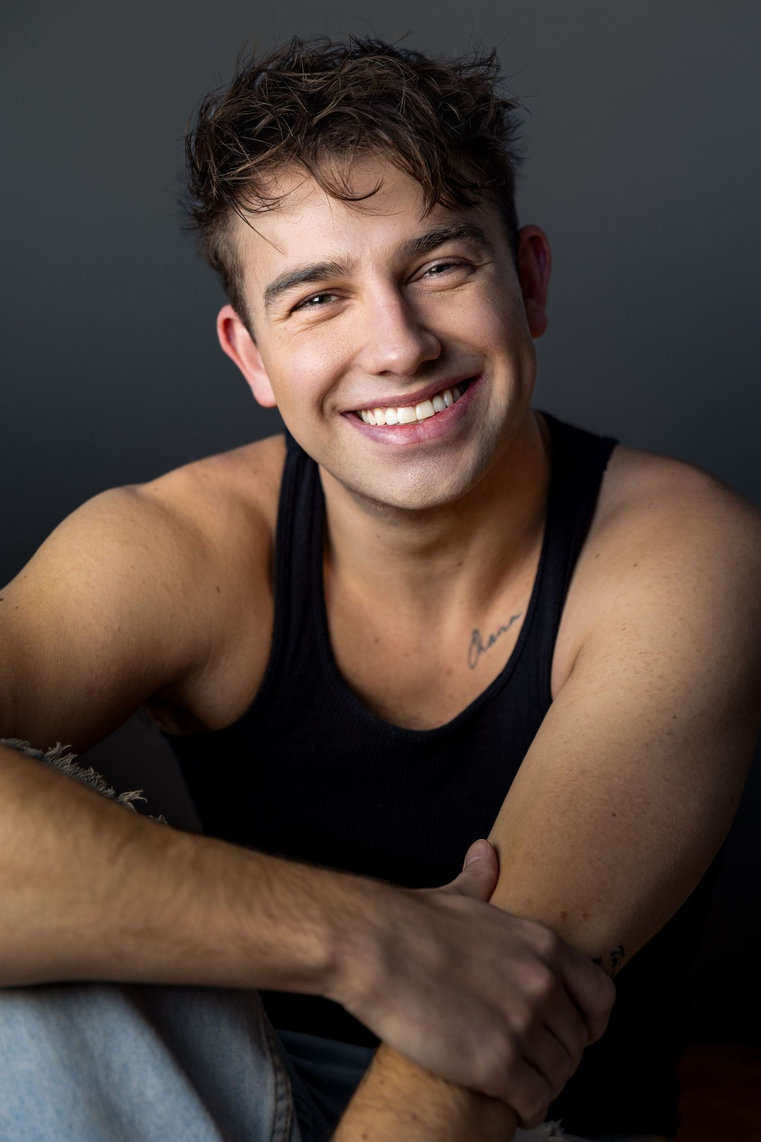 Casual portrait of person in black tank top with natural lighting and dark background.