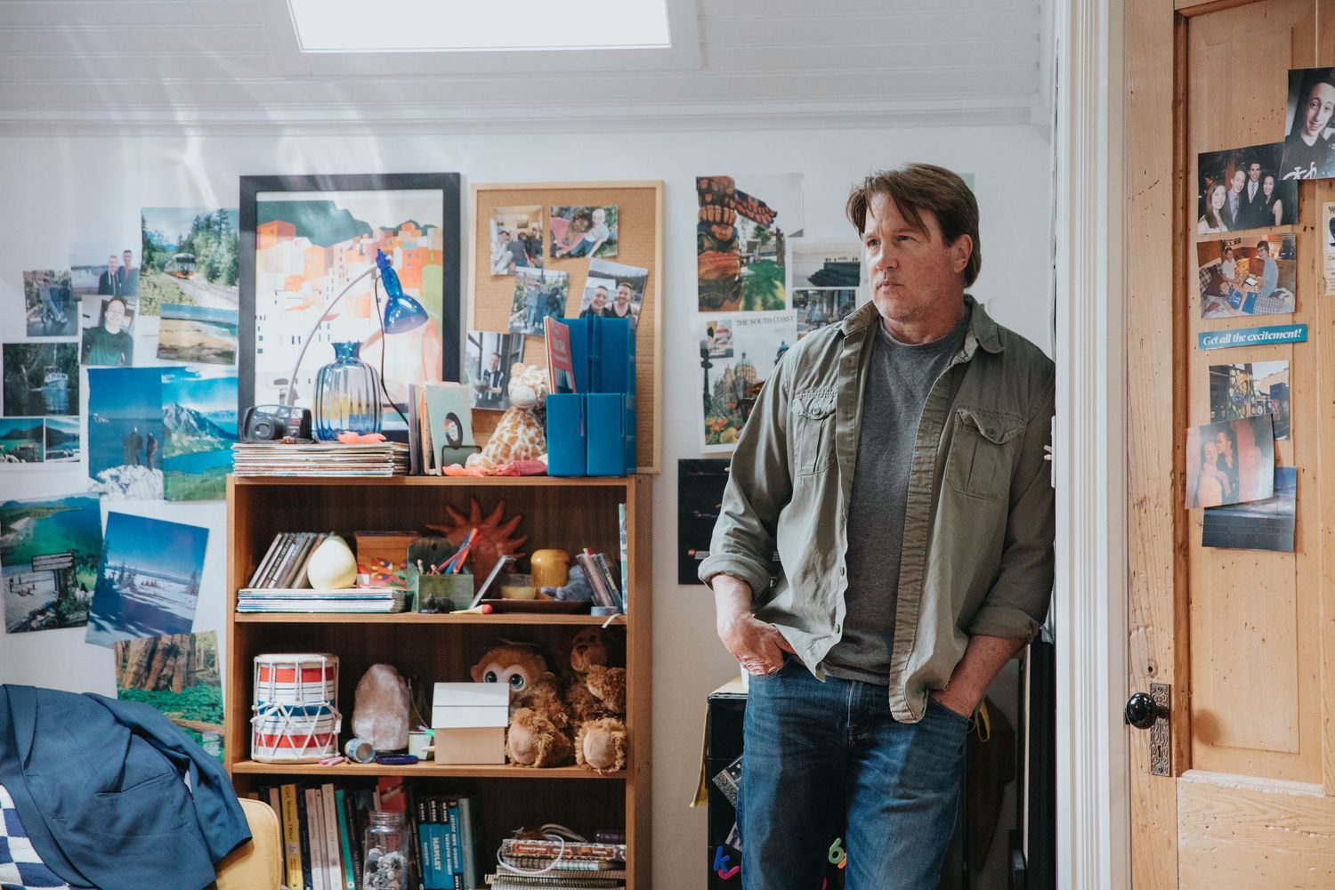 Middle-aged man stands in a creative studio space surrounded by colorful artwork and shelves.