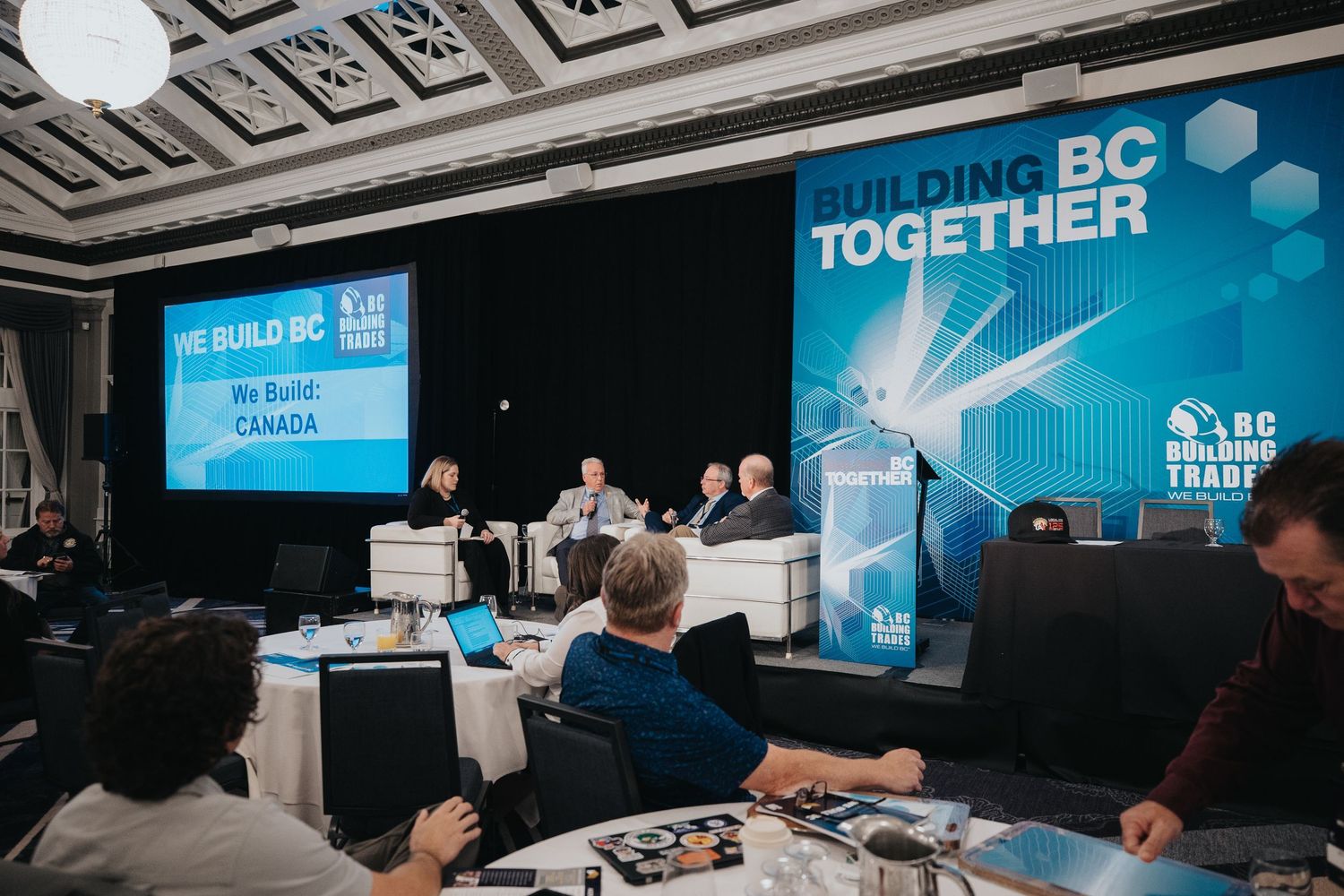 Panel discussion at BC Building Trades 'Building BC Together' conference with speakers on stage and audience members seated.