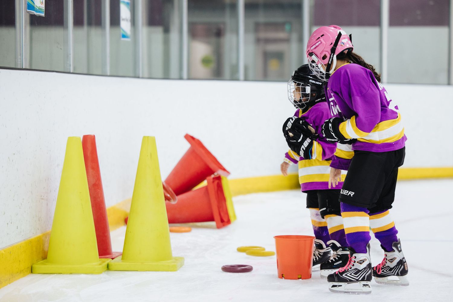 Hockey players in protective gear practice skating around orange cones on ice.