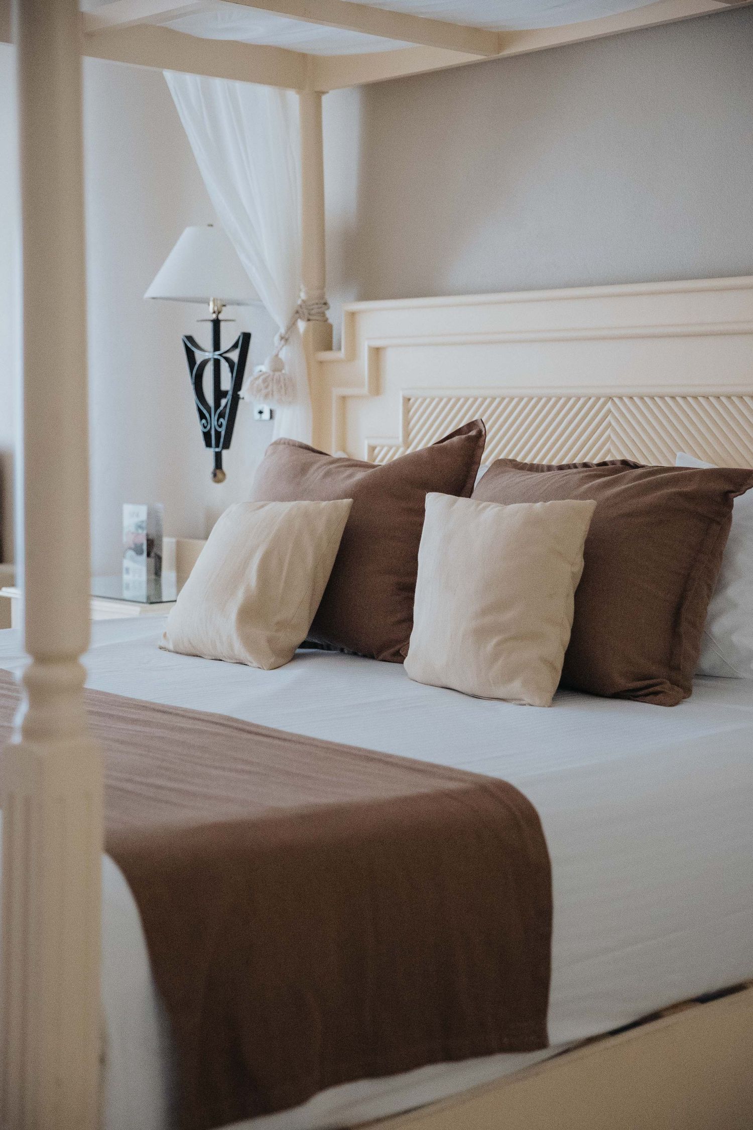 Elegant hotel bedroom with white and brown bedding and decorative pillows.