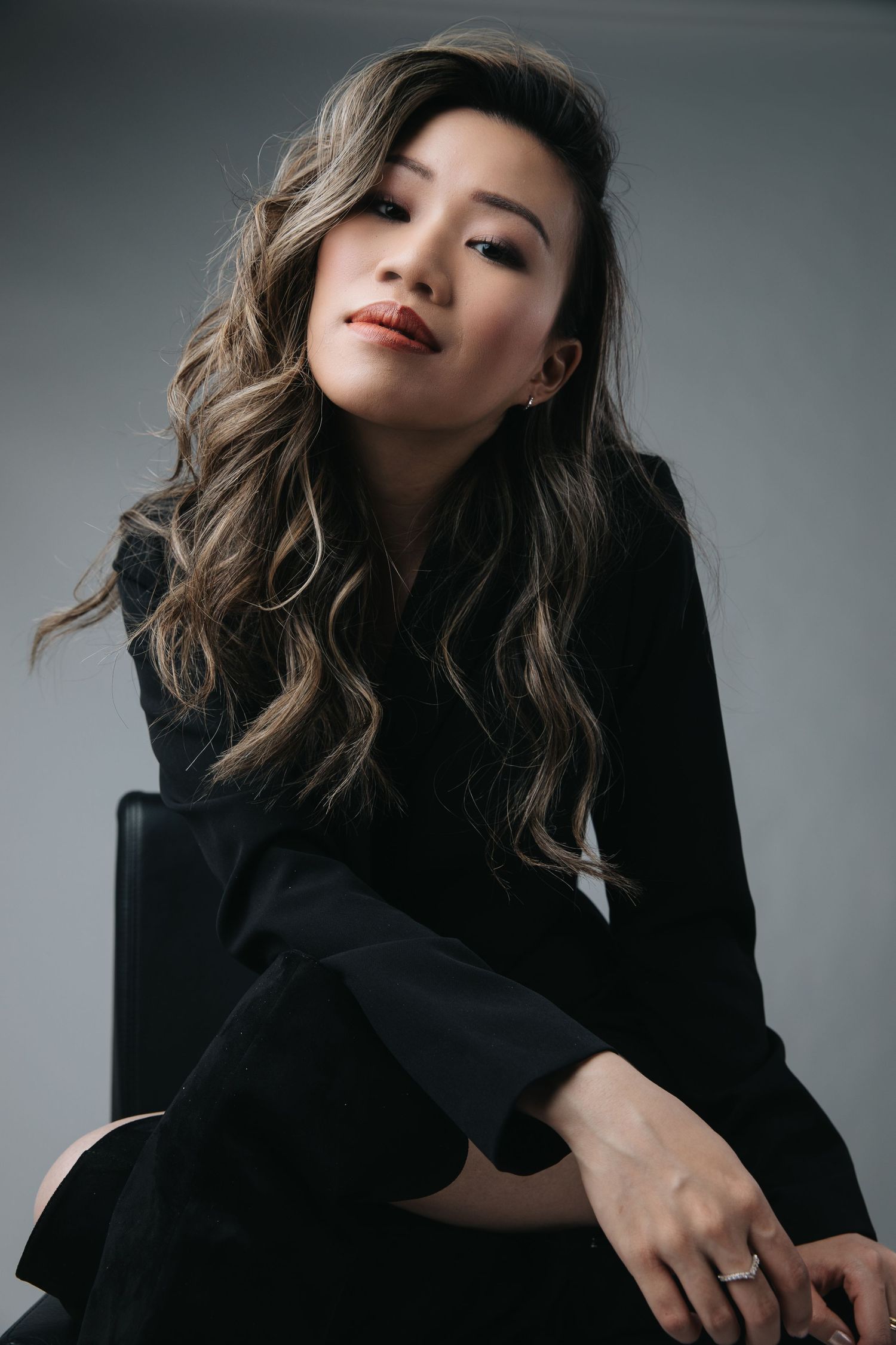Fashion portrait of person in black outfit with styled waves against gray background.