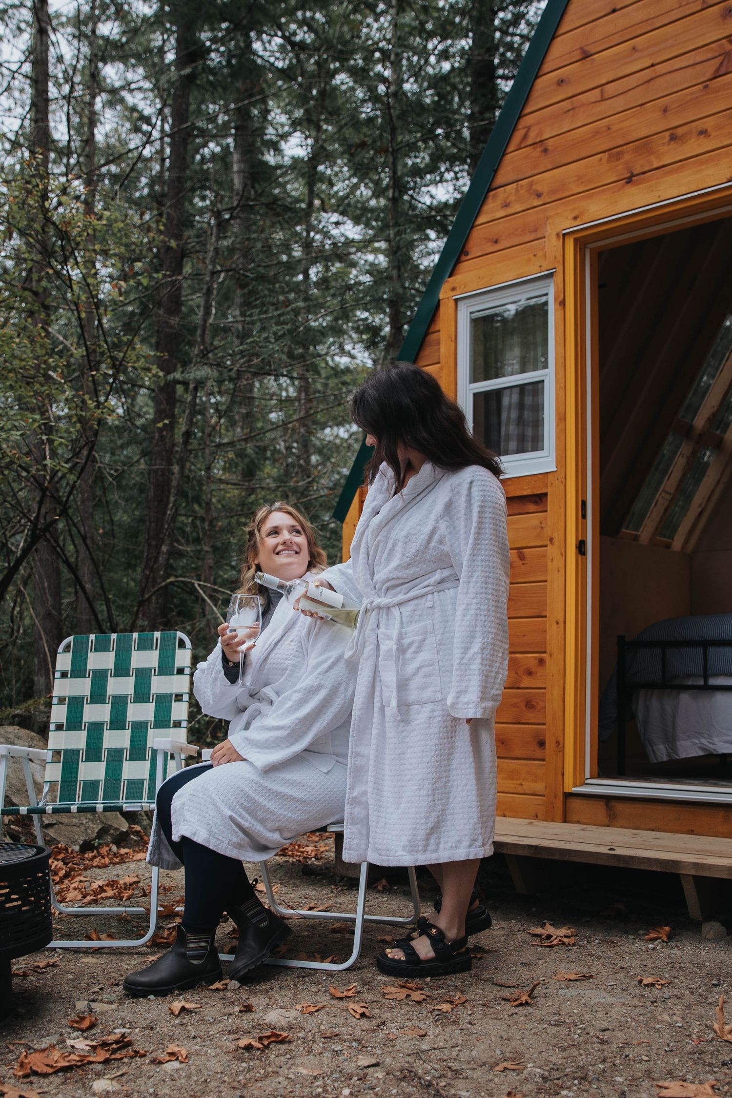 People in white robes relaxing outside rustic cabin in wooded setting.