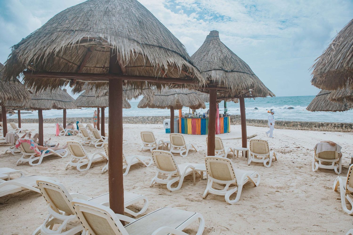 Tropical beach resort with thatched umbrellas and white lounge chairs on sandy shore.