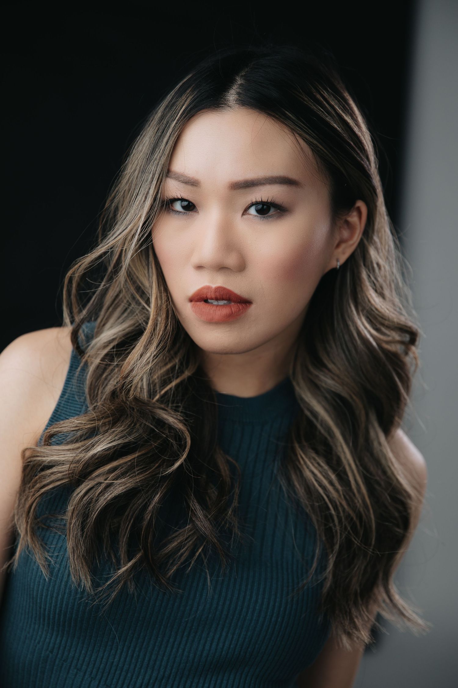 Portrait of person with wavy highlighted hair wearing navy ribbed top against light background.