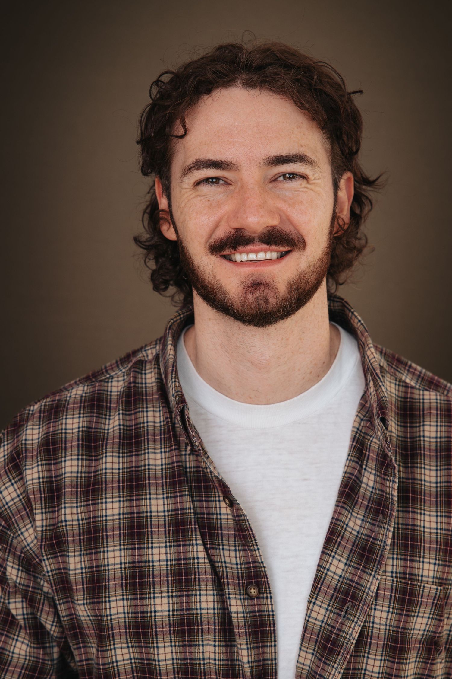 Portrait series featuring warm expressions in a plaid shirt against a dark brown background.