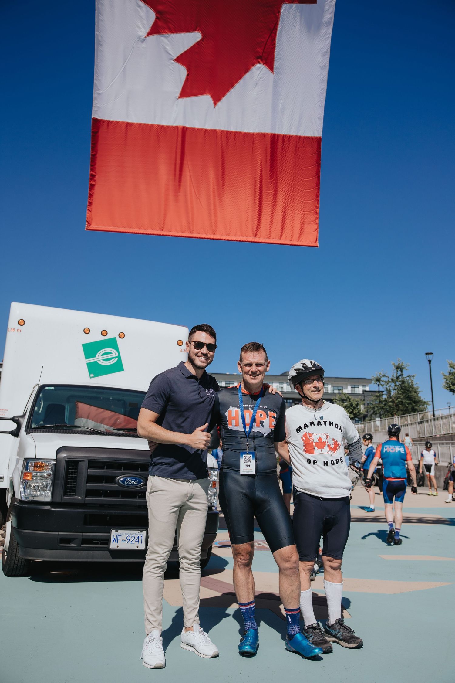People posing together under Canadian flags at an outdoor sporting event.