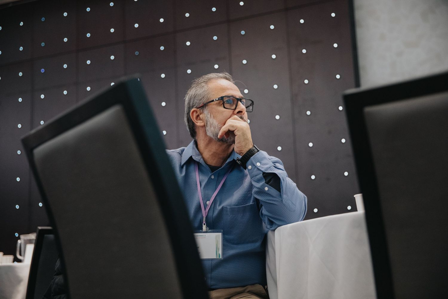 Person in glasses sits at desk in front of dark wall with illuminated dots creating a modern office environment.