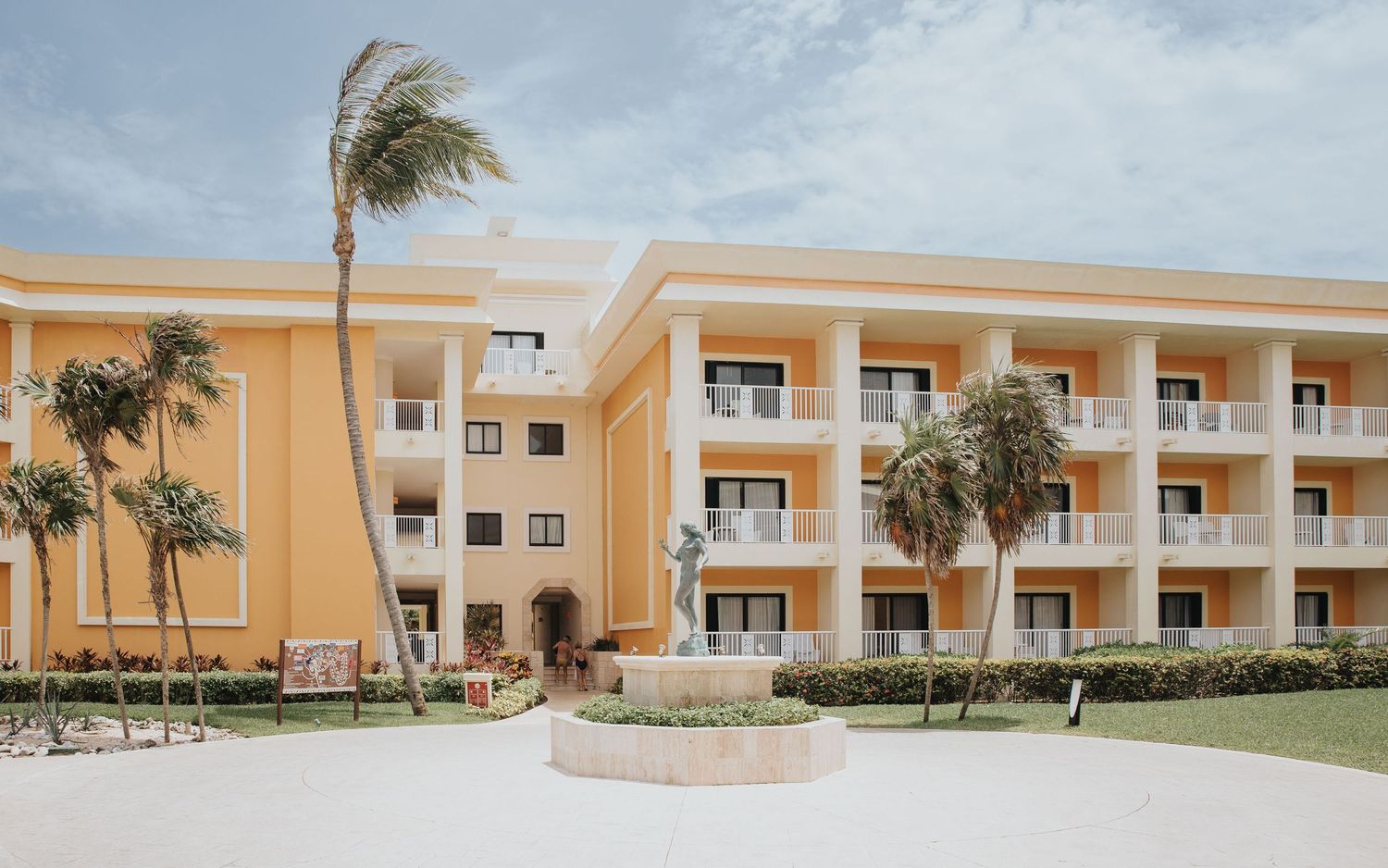 Beige coastal apartment building with palm trees and beachfront view.