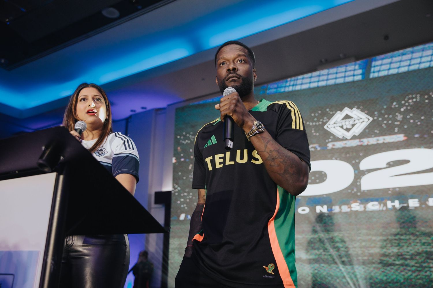 Gaming event presentation with speakers on stage and large projection screen in background.