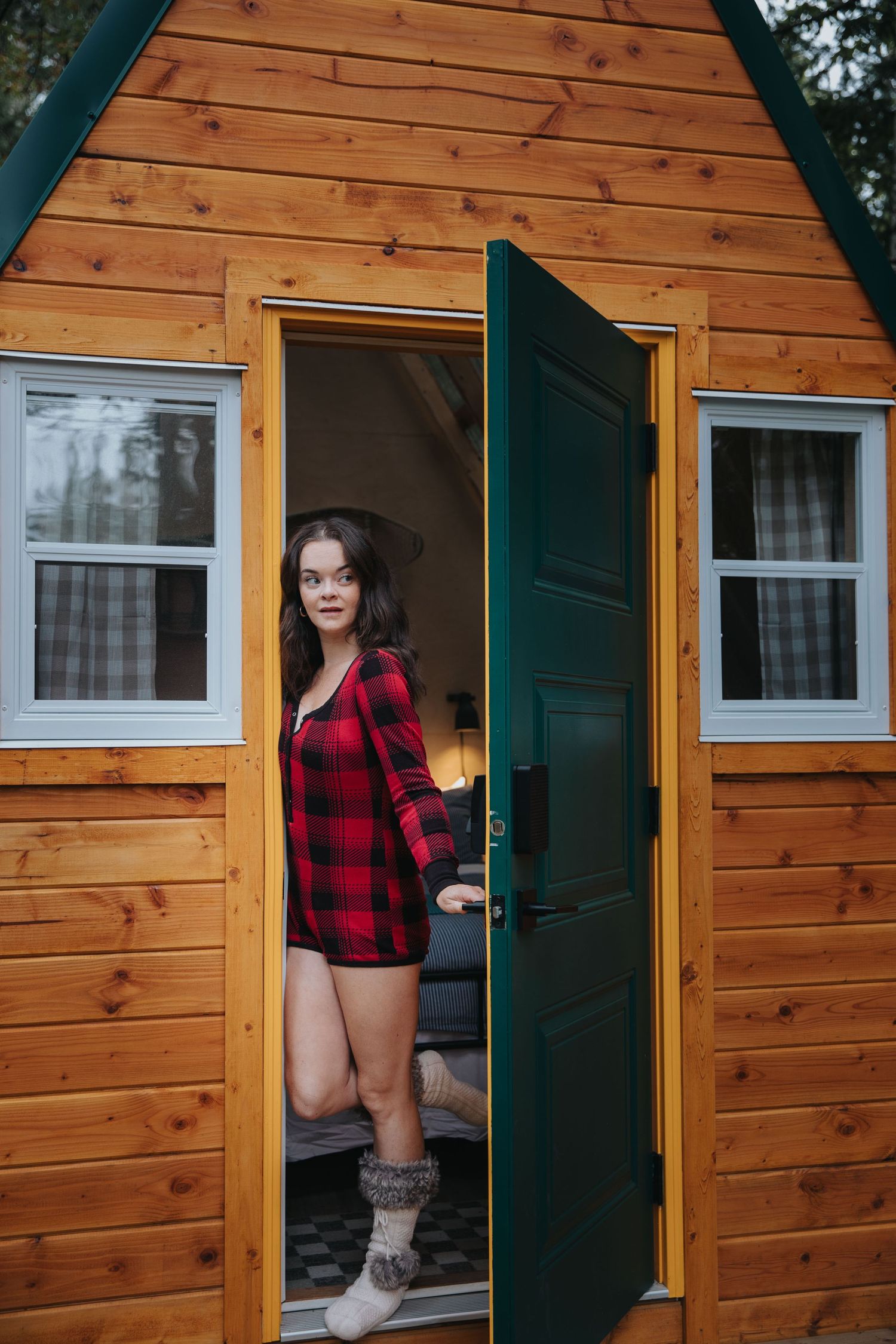 Person in red plaid shirt entering wooden cabin with green trim.