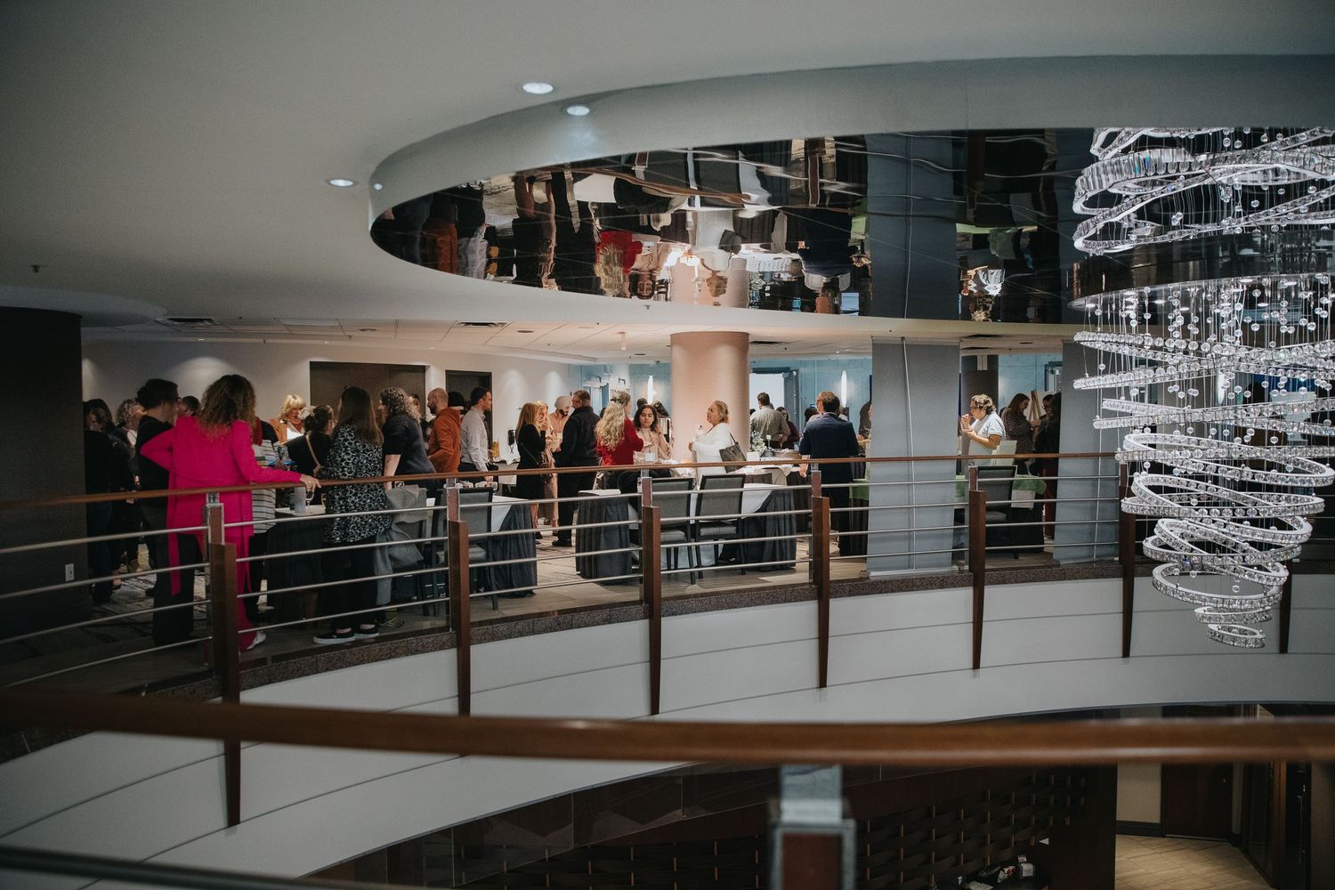 Modern building interior with curved walkways and people gathering on multiple levels.